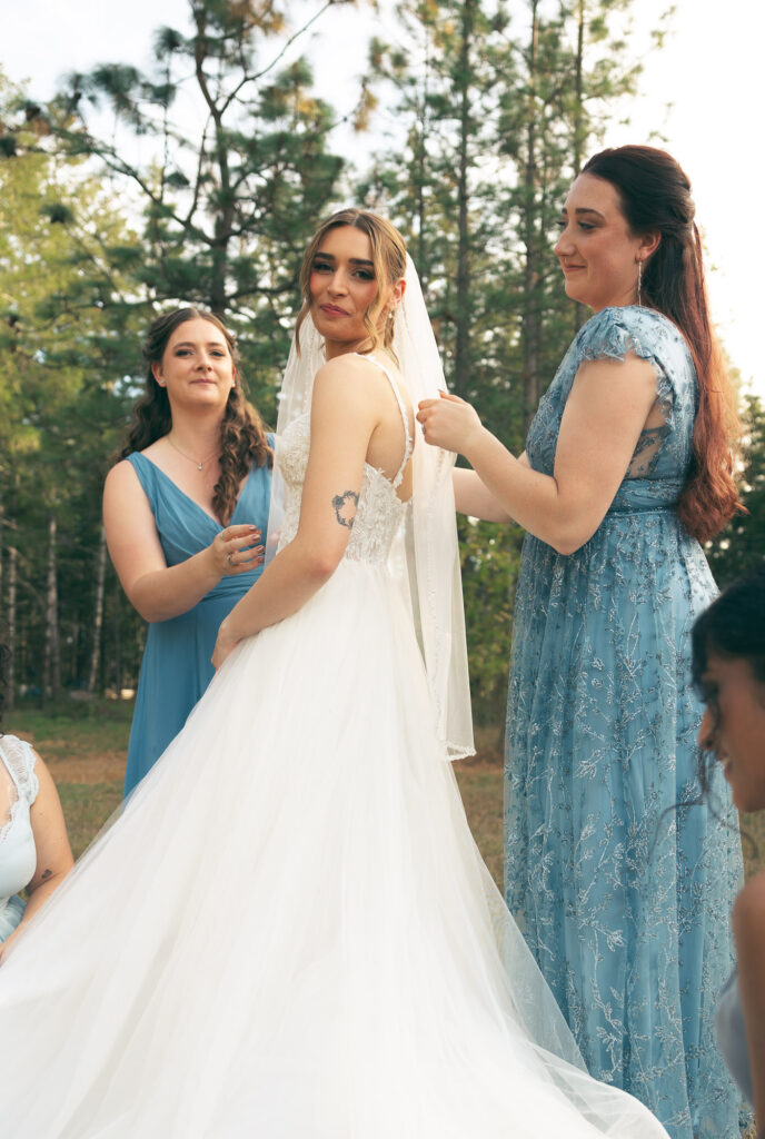 the bride looking at the camera as her bridesmaid get her ready