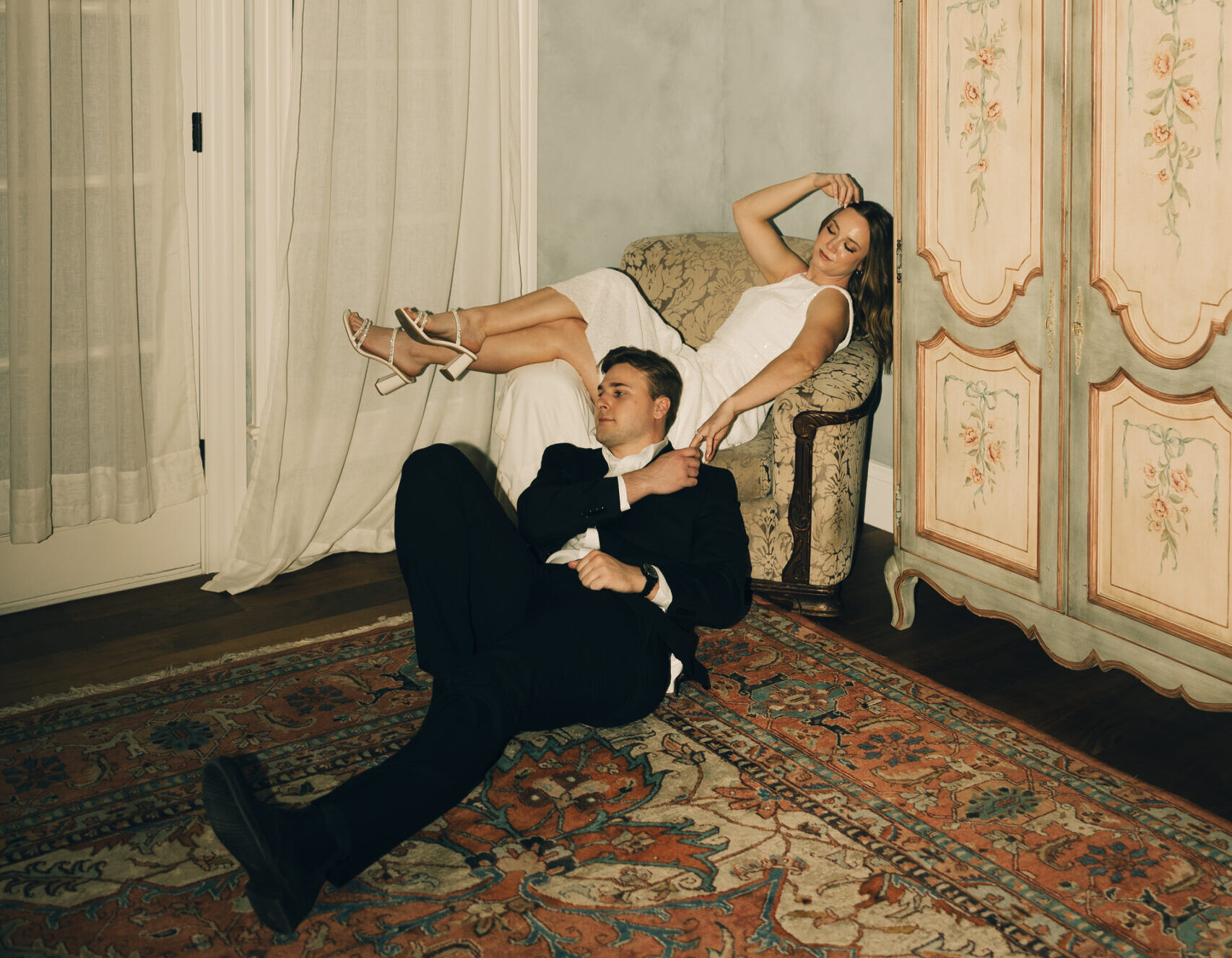 bride lounging on chair and groom laying on floor before her