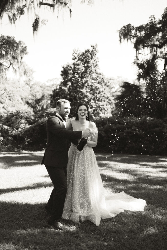 black and white photo of bride and groom popping champagne