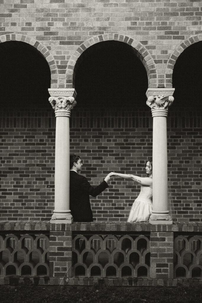 wedding couple leaning on columns and groom looking at bride's rings