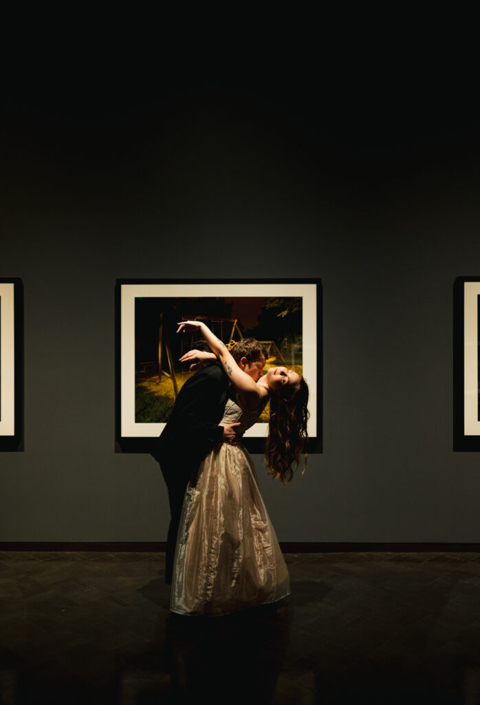 bride leaning back as groom kisses her neck in front of art