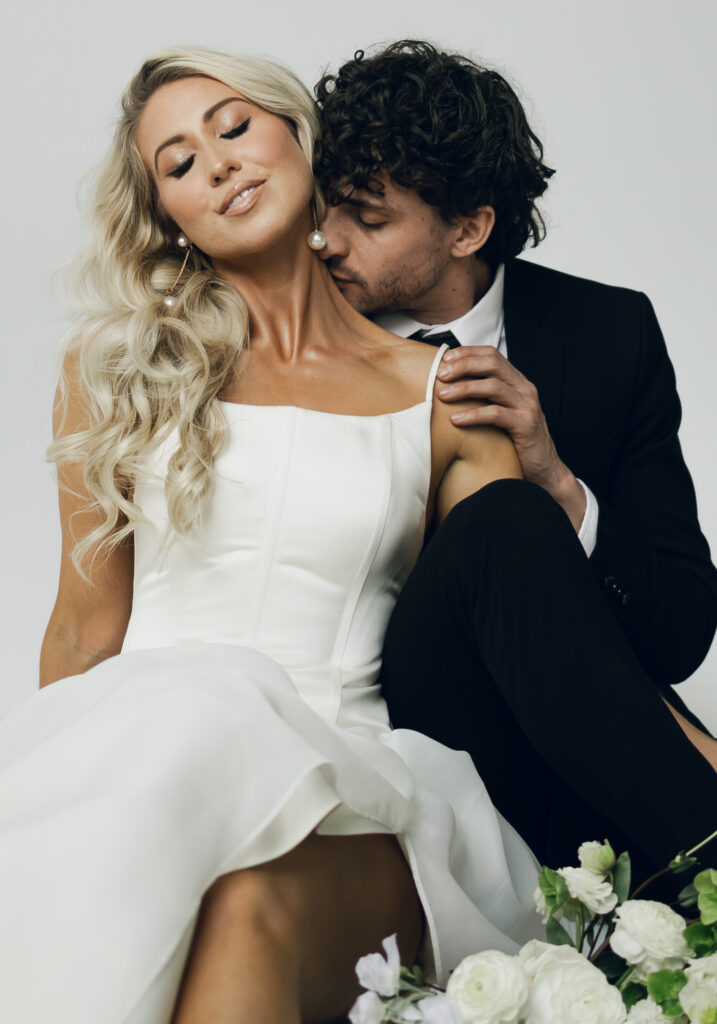 bride sitting between groom's legs and groom kissing her neck