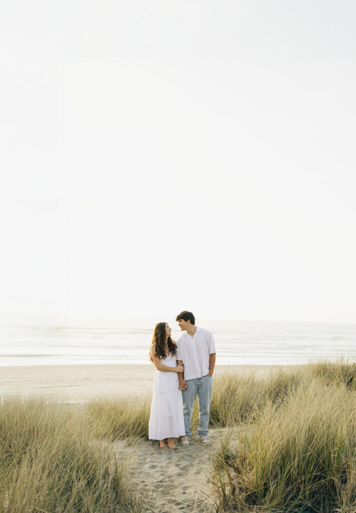 couple facing camera but looking at each other for beach engagement photos