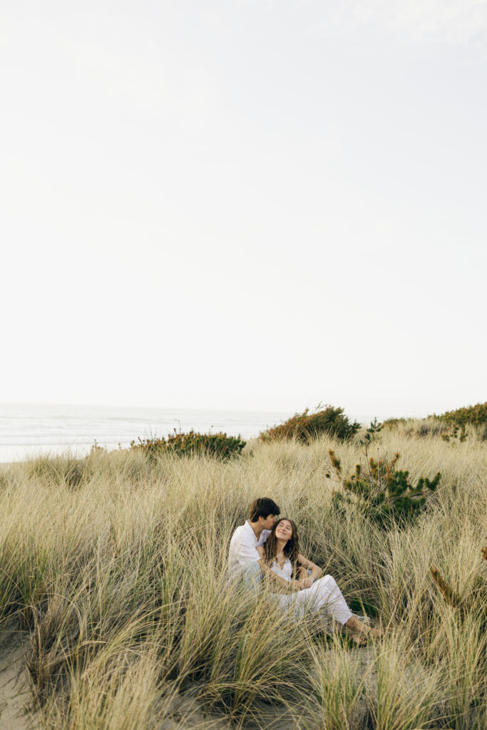 engaged couple sitting in grass at beach