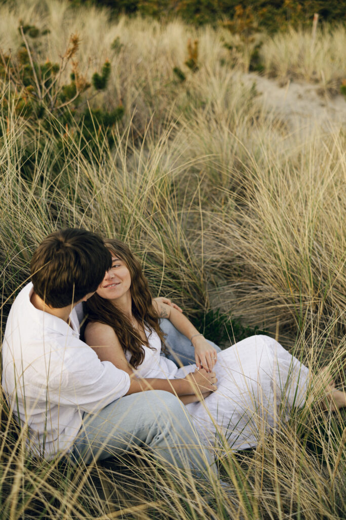 engaged couple sitting in grass at beach