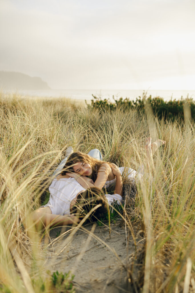 engaged couple laying in grass at beach
