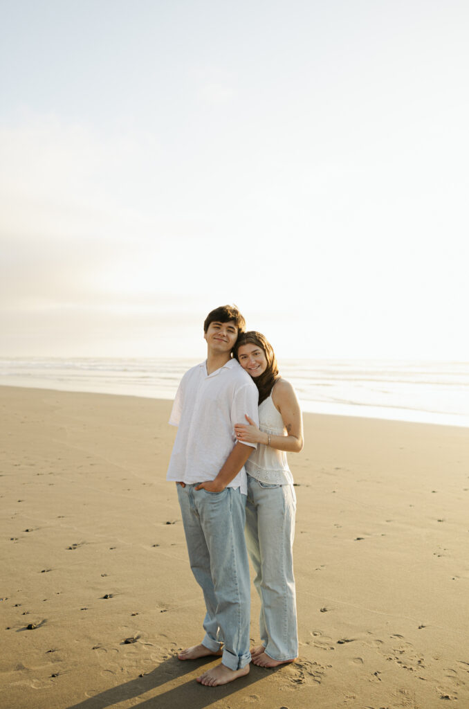 couple standing on beach with girl behind guy and smiling at camera