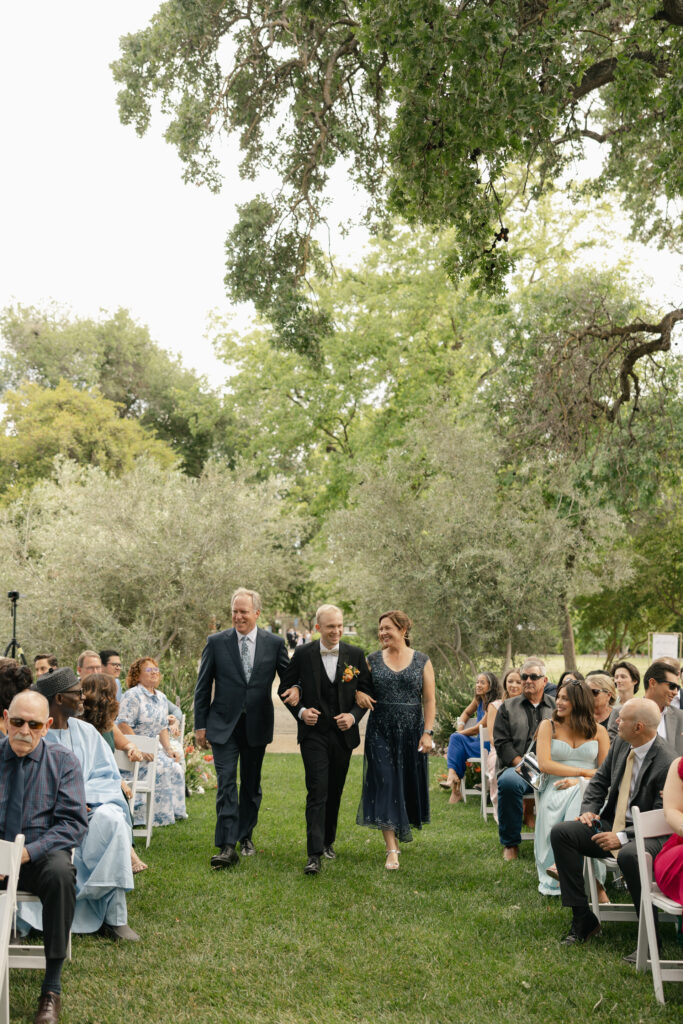 groom with his parents walking down the aisle