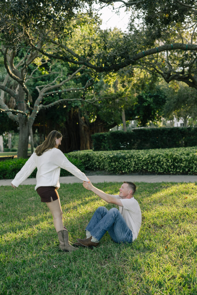 girl helping guy up from sitting in park
