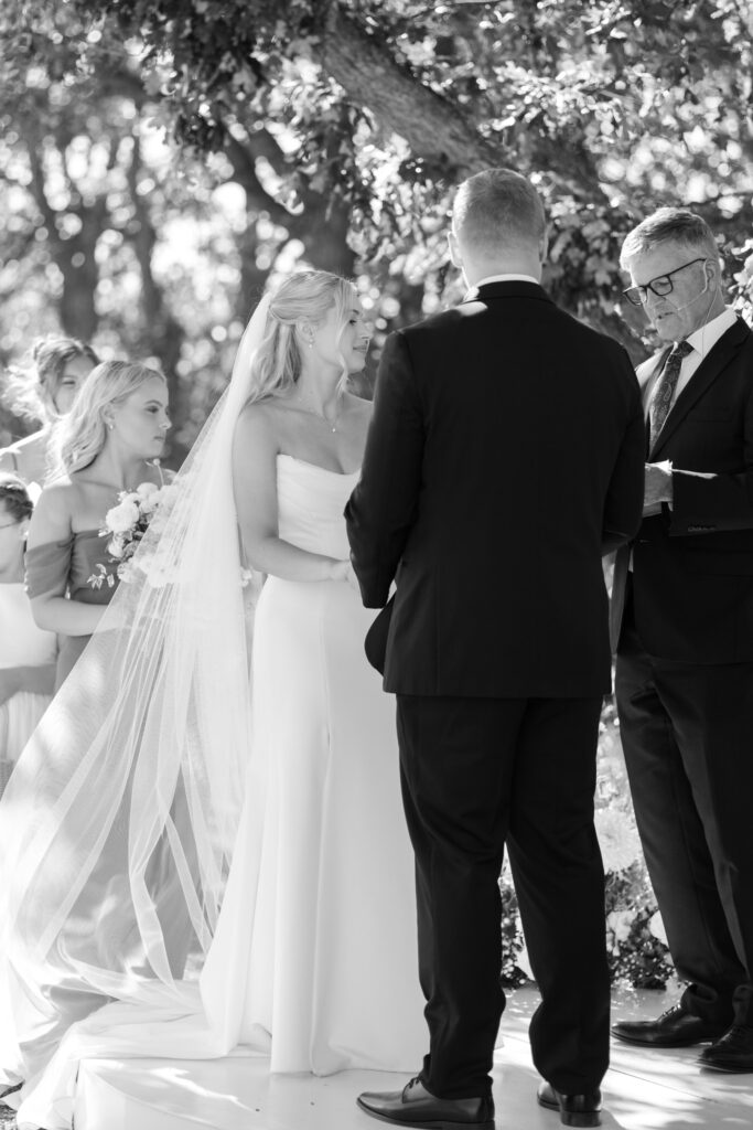 Black and white image of bride and groom looking at officiant during wedding ceremony