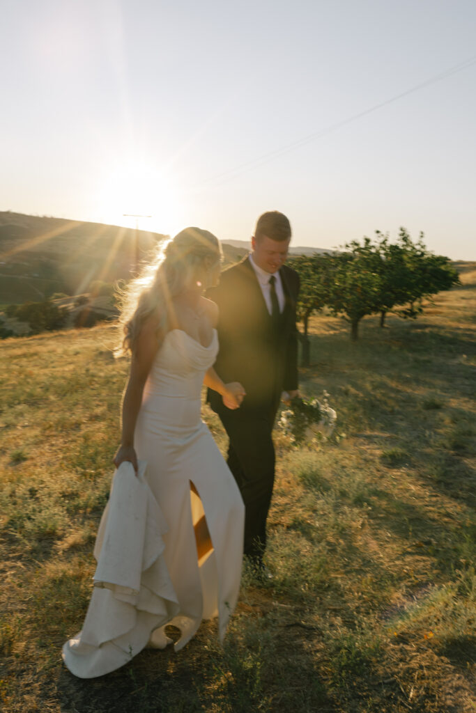 bride and groom walking through orchard during sunset