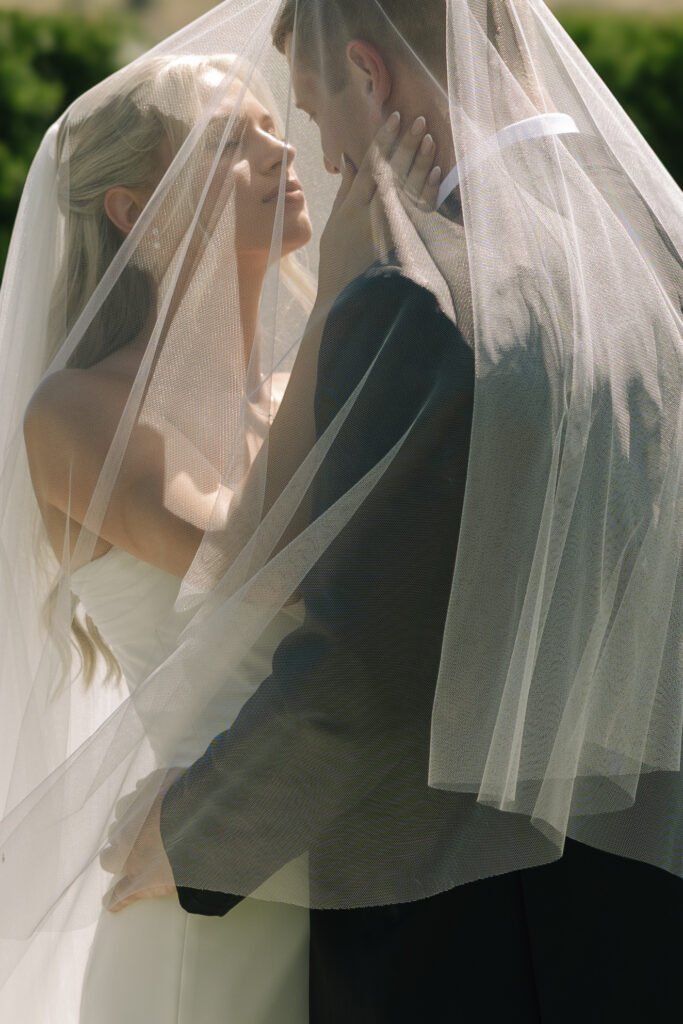 wedding veil draped over bride and groom as they embrace