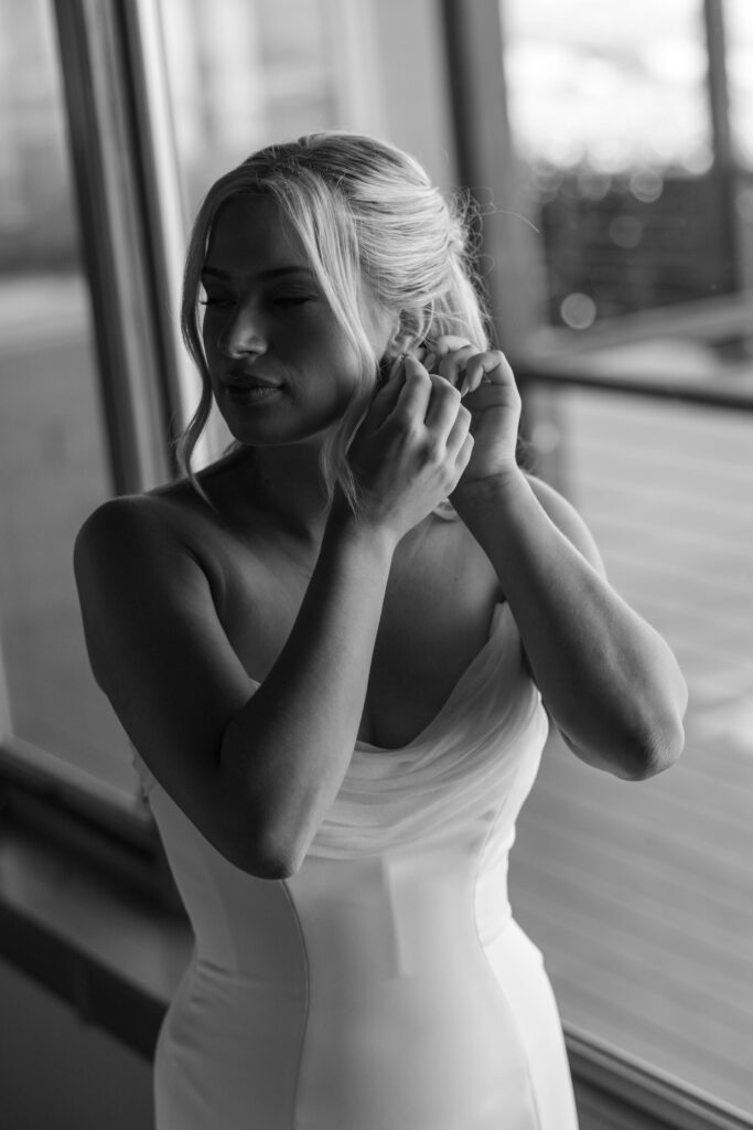 bride putting her earrings on in black & white