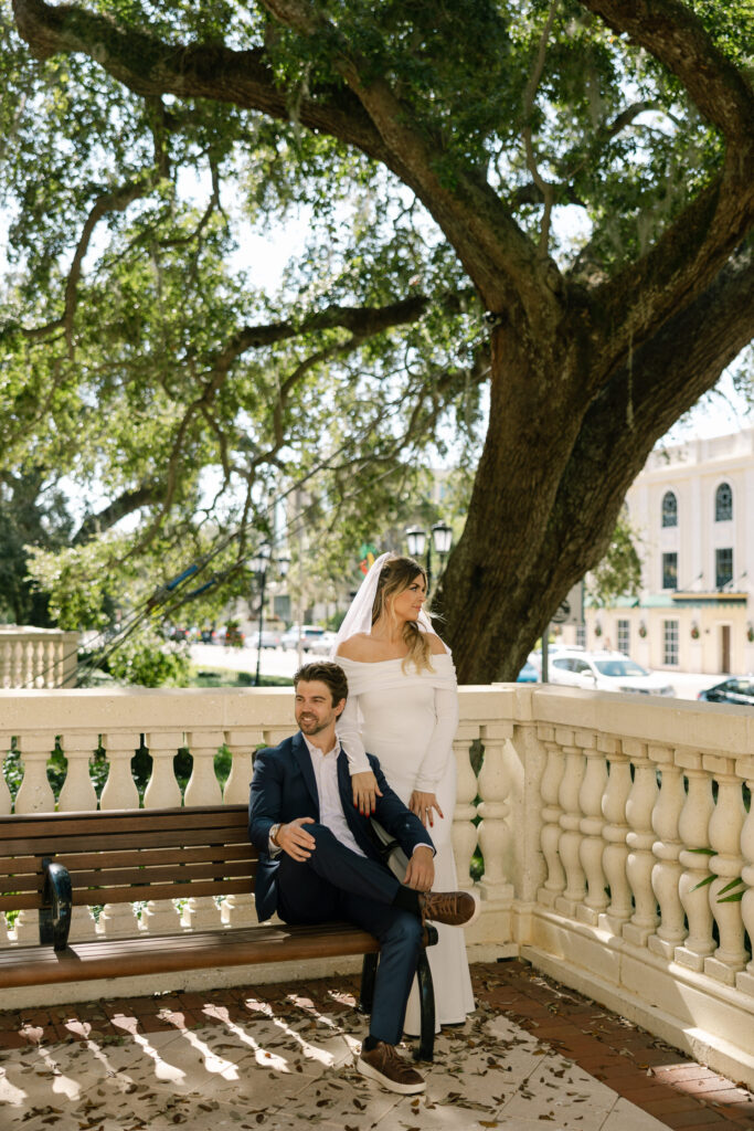 groom sitting on bench with bride standing beside him after clearwater courthouse wedding